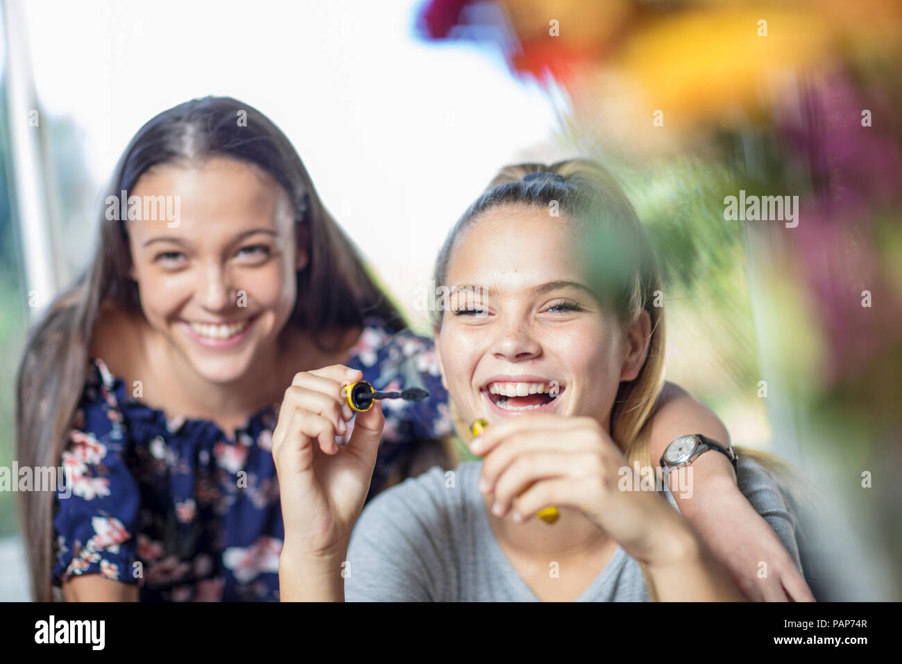 Happy teenage girl watching friend applying mascara Stock Photo