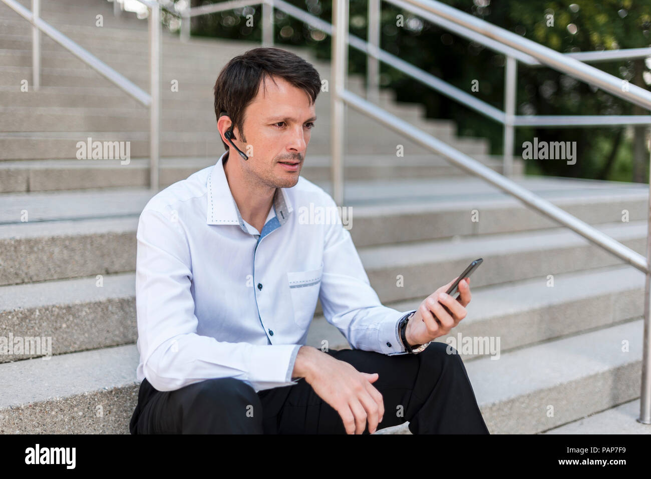 Businessman with headset and cellphone sitting on stairs Stock Photo
