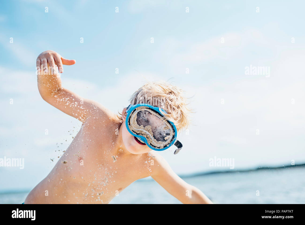 Boy with diving goggles on the beach playing with sand Stock Photo