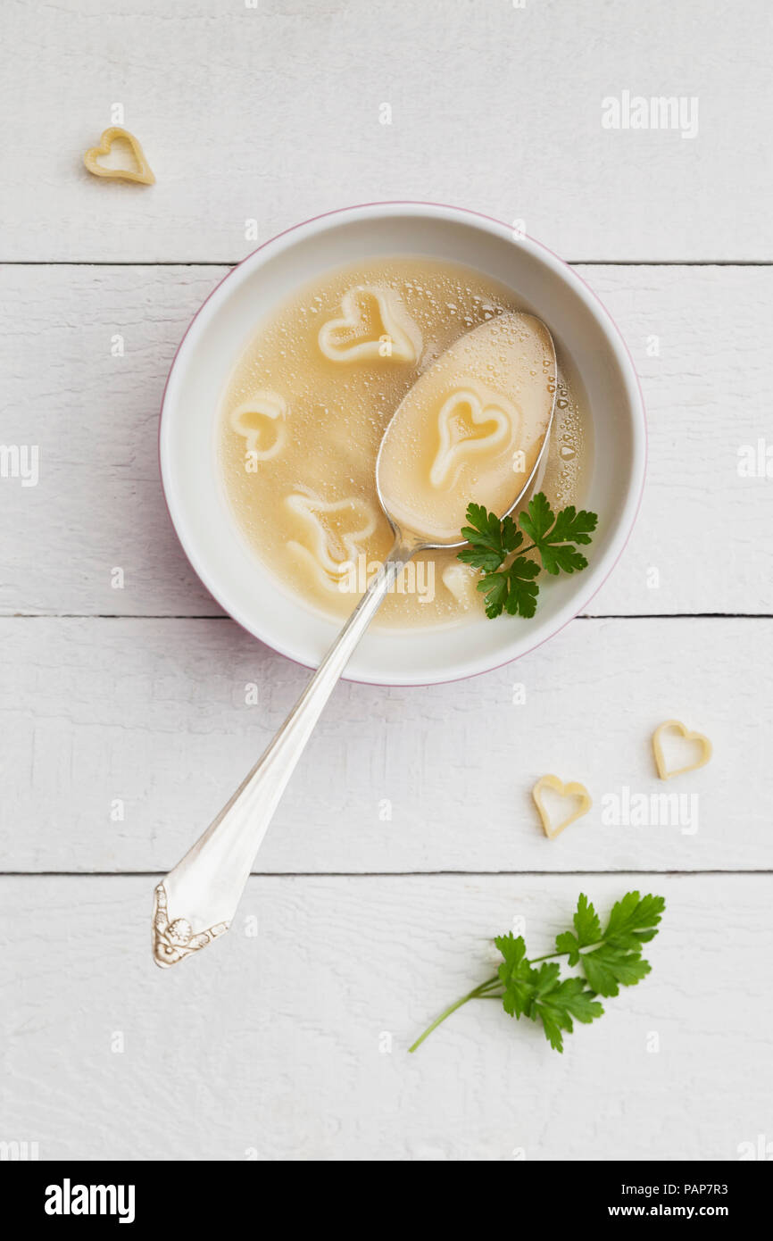 Silver spoon in bowl of chicken soup with heart-shaped noodles and parsley Stock Photo