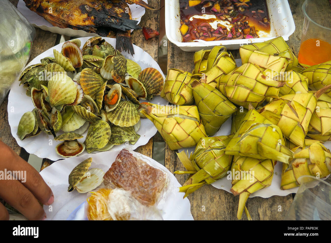Filipino seafood &picnic food consisting of Clams, Fried fish, hanging rice (puso) at a beach party - Bantayan Island, Cebu - Philippines Stock Photo