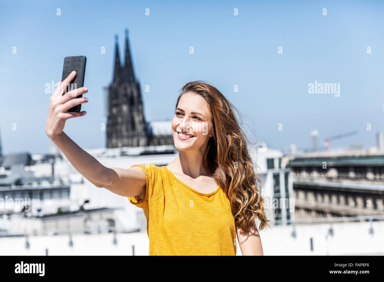 Germany, Cologne, portrait of smiling woman taking selfie with smartphone on roof terrace Stock Photo