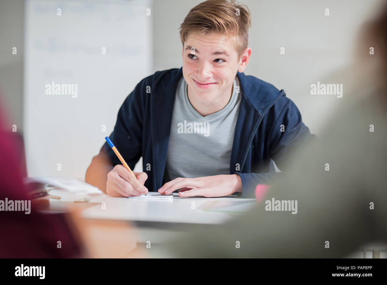 Smiling teenage boy taking notes in class Stock Photo