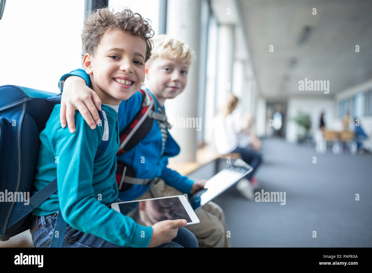 Portrait of two smiling schoolgboys with tablet embracing Stock Photo
