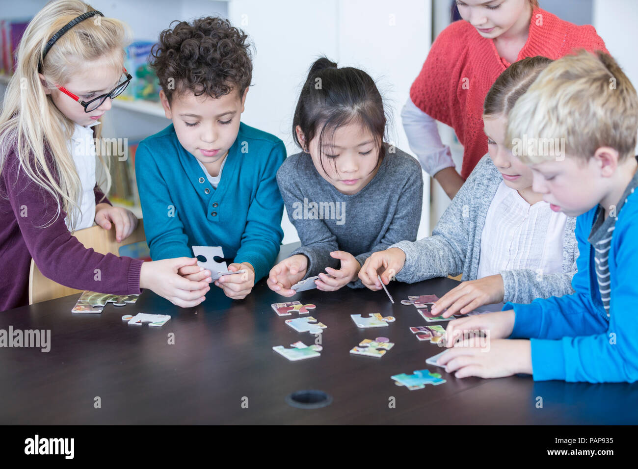 Pupils playing jigsaw puzzle in school together Stock Photo