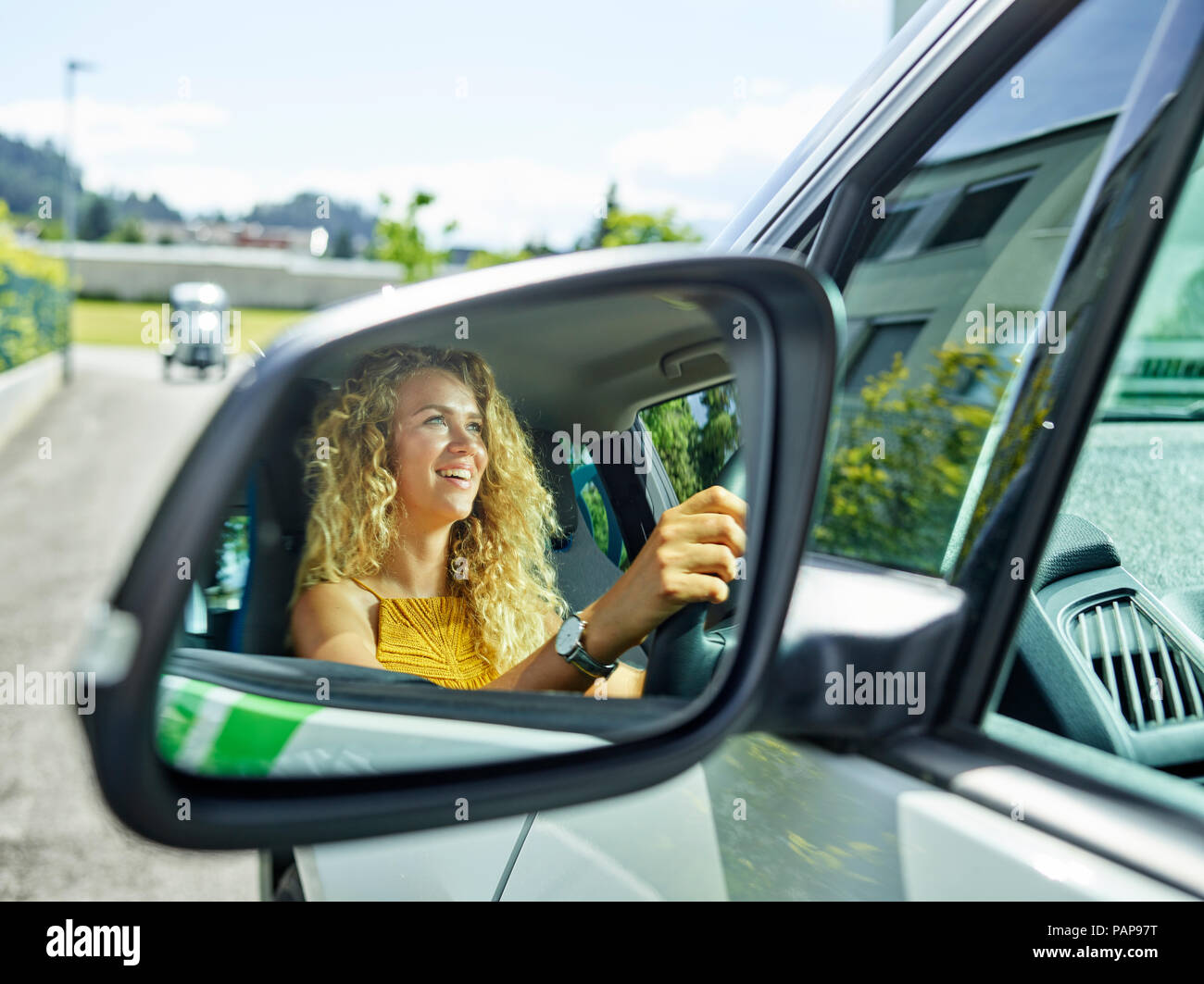 Reflection in wing mirror of smiling woman driving electric car Stock Photo