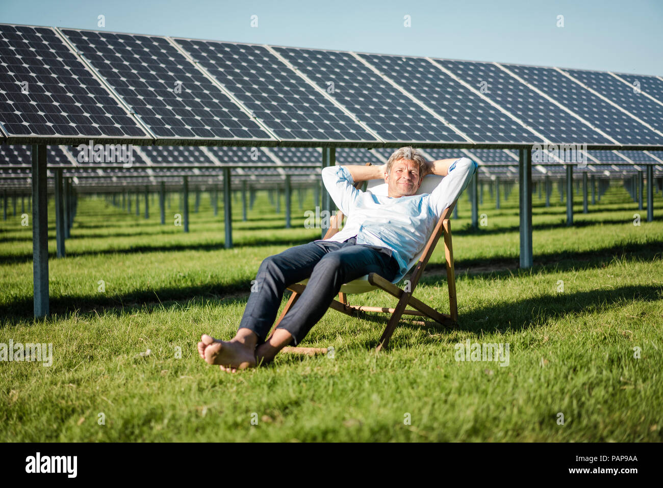 Mature man sitting in sun lounger, solar plant Stock Photo