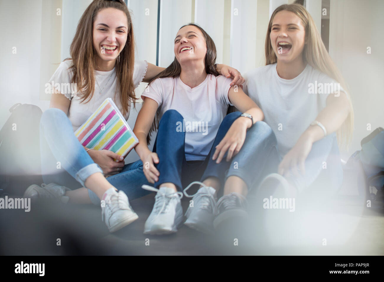 Happy teenage girls sitting on floor in school Stock Photo