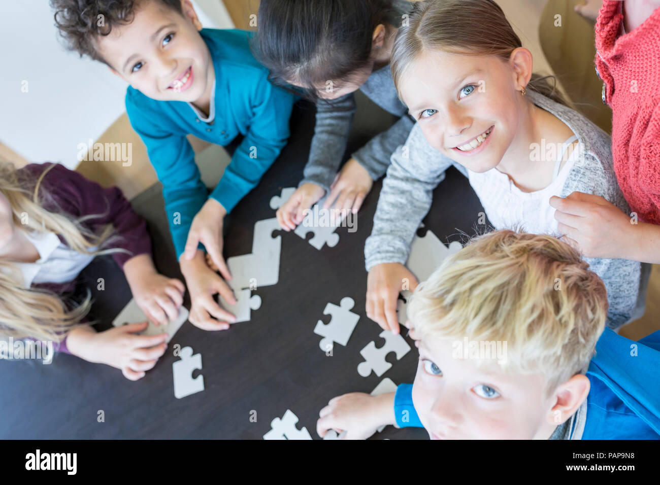 Portrait of smiling pupils playing jigsaw puzzle in school together Stock Photo