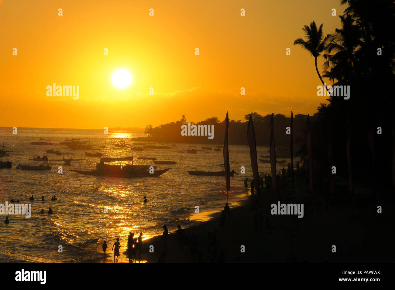 Beautiful golden sunset over tropical Alona Beach, with tour boat and tourist silhouettes - Bohol, Philippines Stock Photo