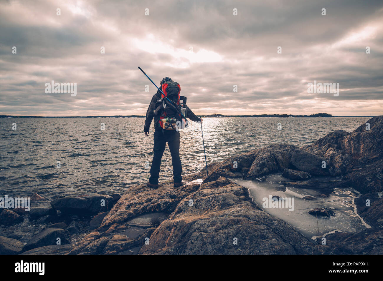 Sweden, Sodermanland, backpacker standing at the seashore under cloudy sky Stock Photo