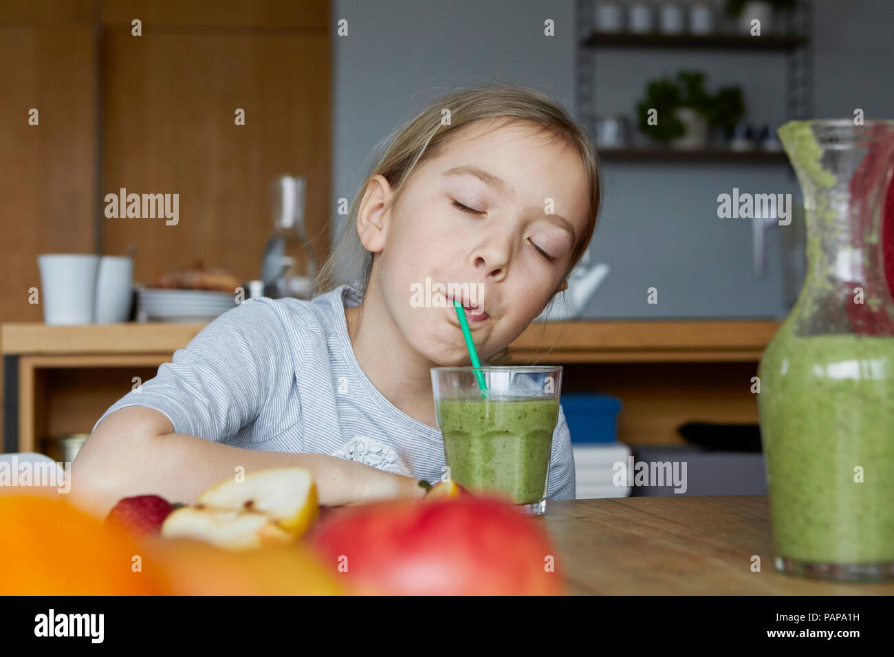 Girl sitting in kitchen, drinking homemade fruit smoothie Stock Photo
