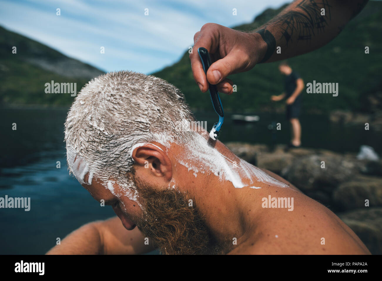 Norway, Lofoten, Traveller getting his head shaved at lake Stock Photo