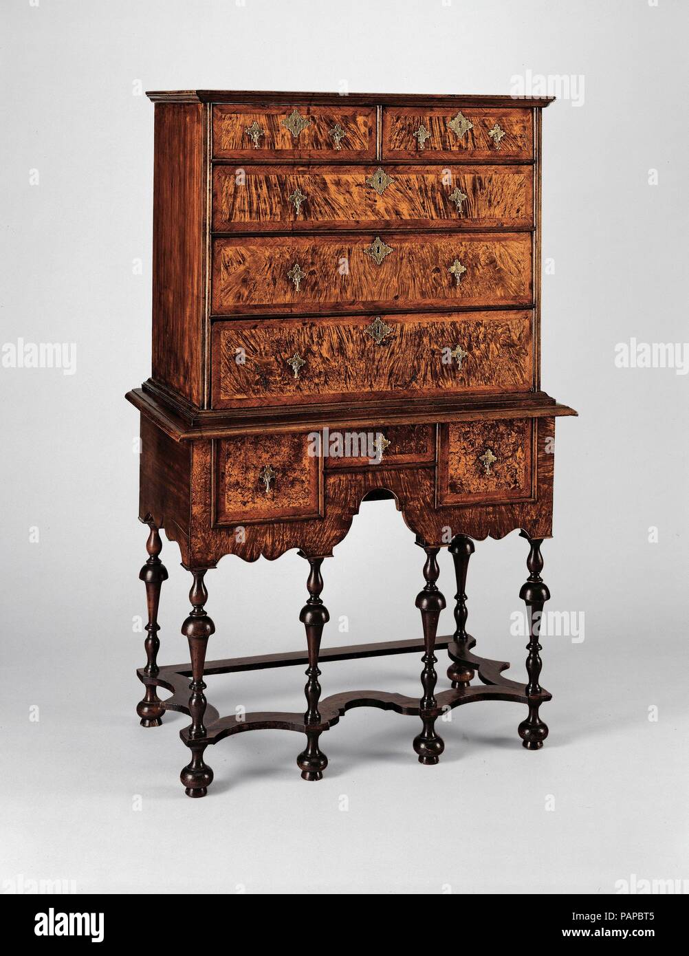 High chest of drawers. Culture: American. Dimensions: 62 1/2 x 39 1/4 x 21 3/4 in. (158.8 x 99.7 x 55.2 cm). Date: 1700-1730.  A new form introduced with the William and Mary style, the high chest of drawers was a prestigious addition to the early-eighteenth-century home. The scalloped skirt, curved stretchers, and six turned legs on this chest bring lightness and movement to the form. The large, smooth surfaces of the drawer fronts of the upper and lower cases were achieved by abandoning the panel-and-frame tradition in favor of dovetailed-board construction--a technique created by the new cr Stock Photo