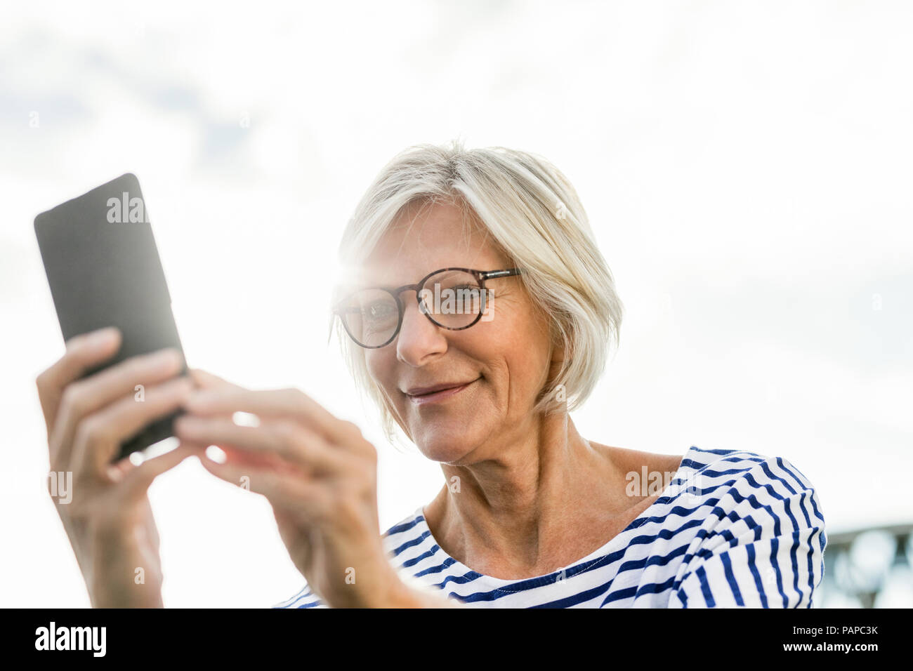 Smiling senior woman using cell phone outdoors Stock Photo