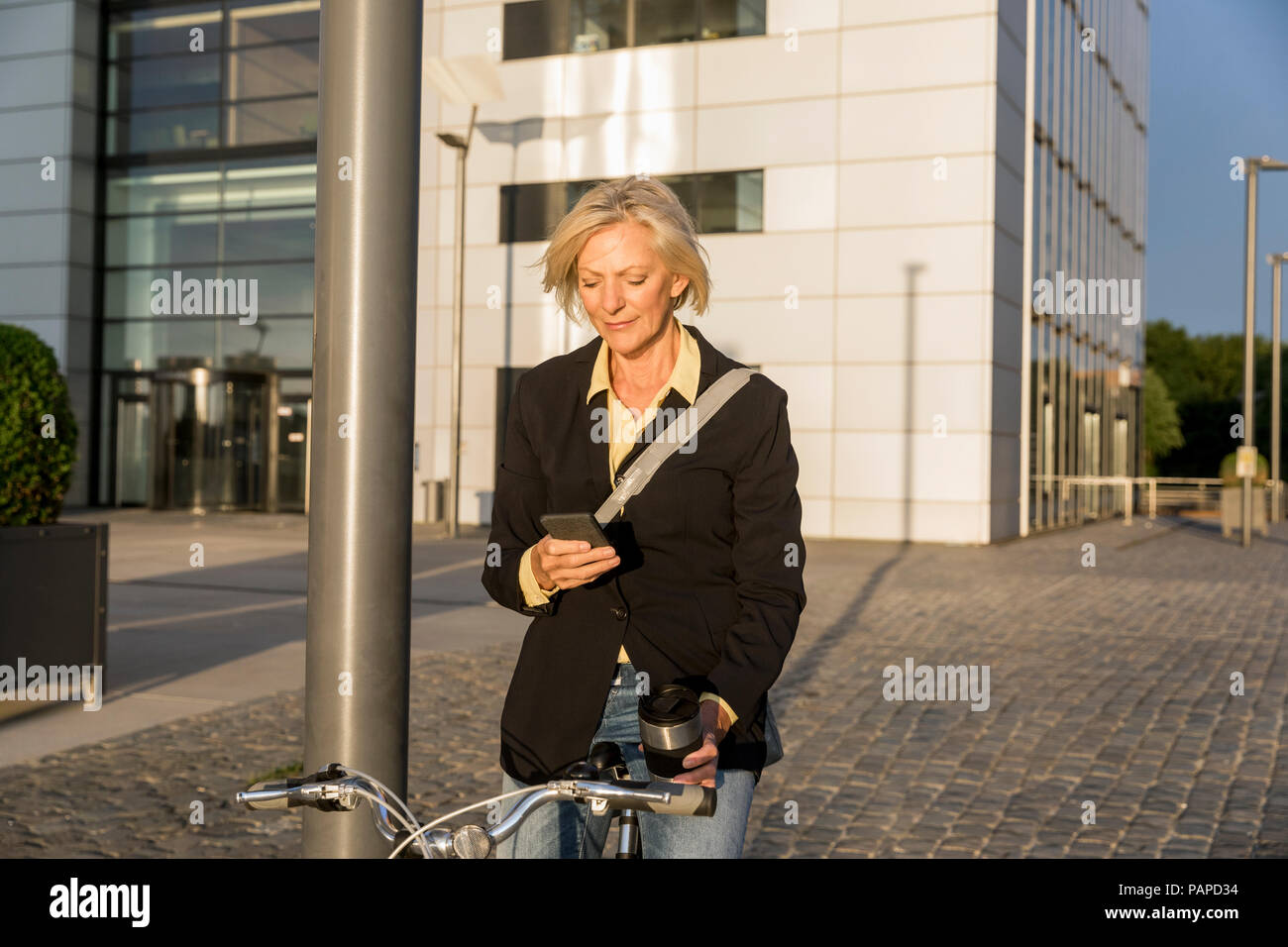 Senior woman with city bike and takeaway coffee using cell phone Stock Photo