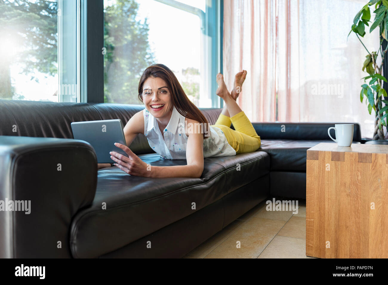 Portrait of happy woman lying on couch at home using a tablet Stock ...