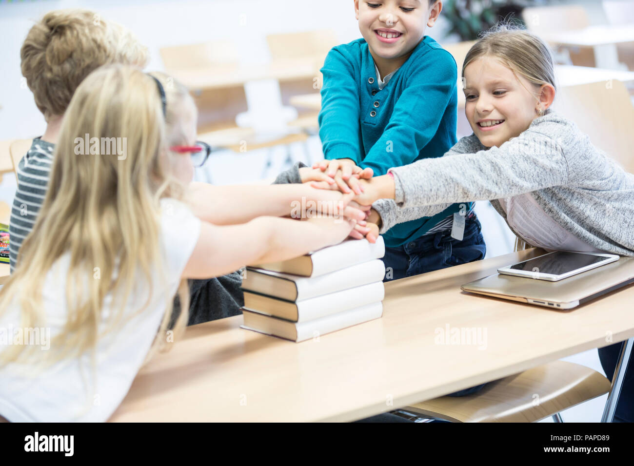 Happy pupils stacking hands on books in class Stock Photo