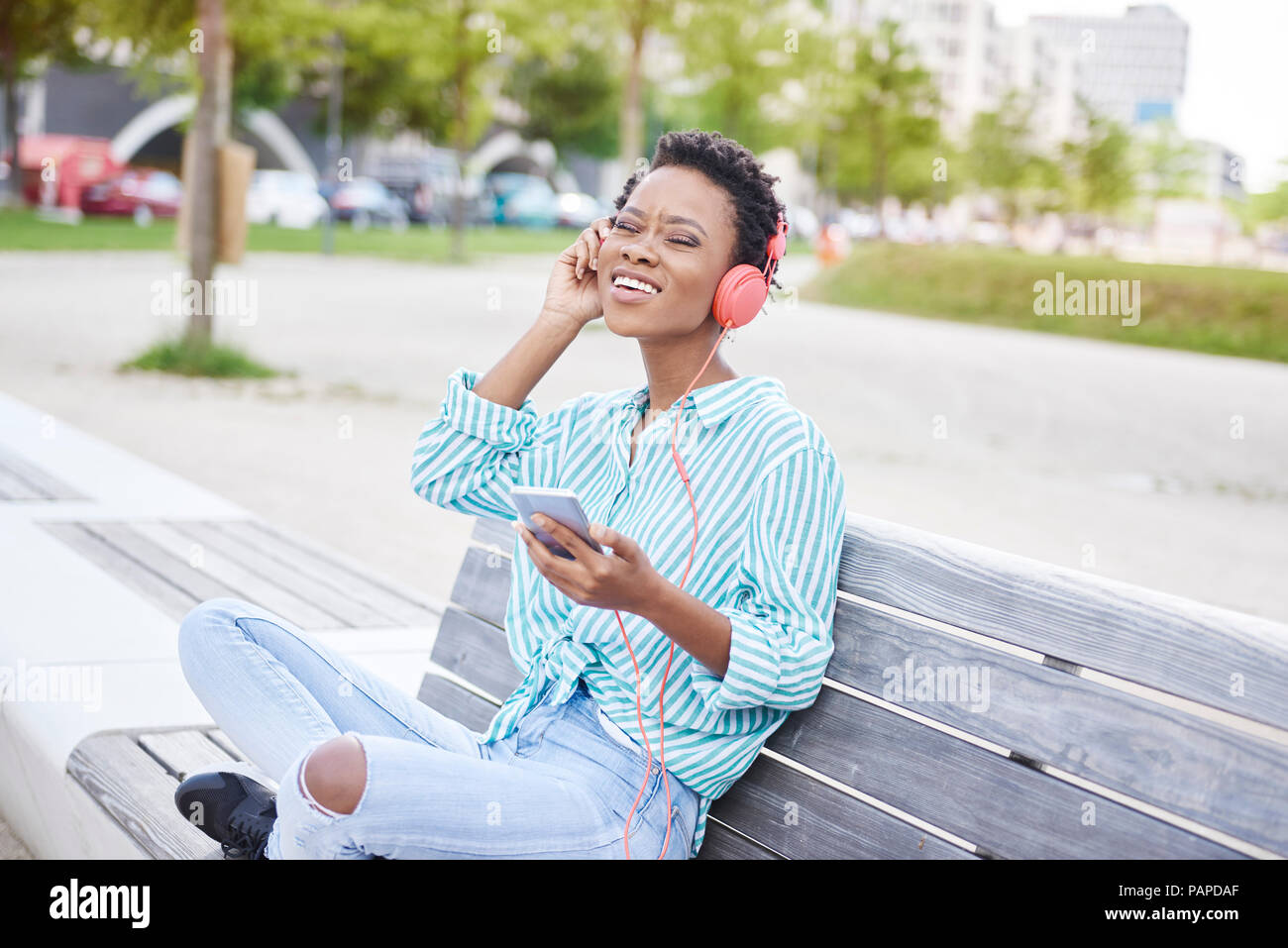 Portrait of young woman sitting on bench listening music with cell phone and headphones Stock Photo