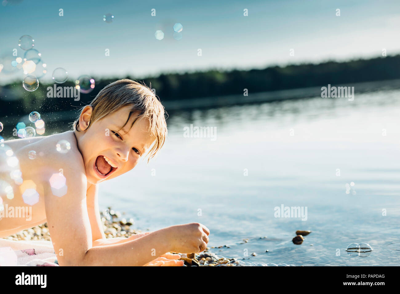 Happy boy at a lake surrounded by soap bubbles Stock Photo
