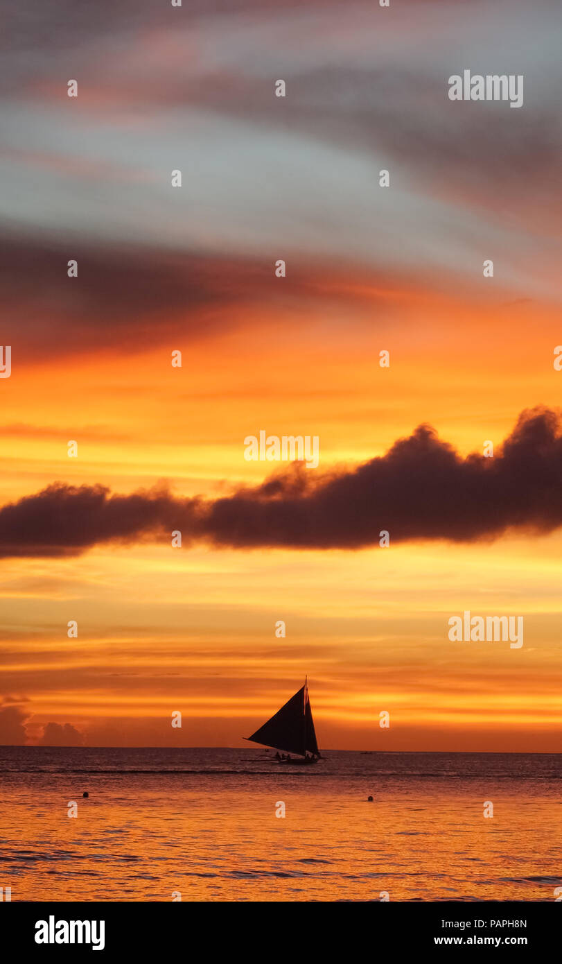 Sailboat silhouette under a dramatic, cloudy orange island sunset  - Boracay, Aklan - Philippines Stock Photo