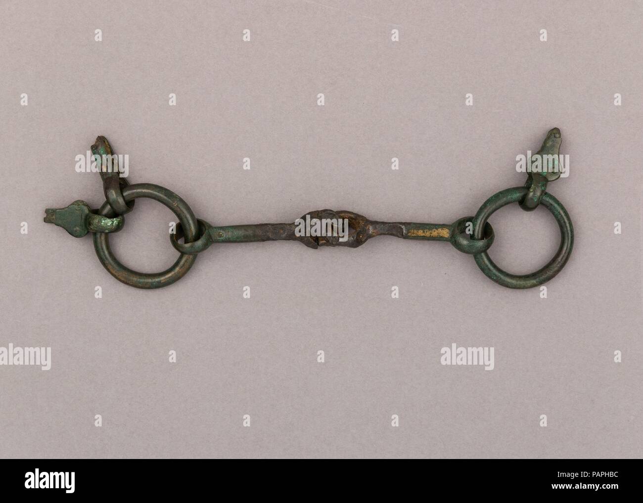 Snaffle Bit. Culture: Italian, Lombardy. Dimensions: W. 6 1/8 in. (15.6 cm); Wt. 7.9 oz. (224 g). Date: 4th-5th century.  The snaffle bit is the simplest type of horse bit, and has an effect on the bars (part of the horses' jaw without teeth) and the corners of the lips. The mouthpiece consists of two square-section canons, half in bronze, half in iron, articulated in the center. The side rings retain the pear-shaped tabs with rivets used for hanging the bit from the bridle and one remaining simple straight tab on one side for attaching one of the reins.  This bit is said to have been found in Stock Photo