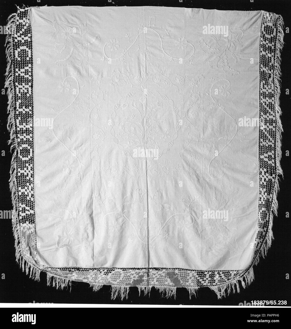 Embroidered whitework coverlet. Culture: American. Dimensions: 83 5/8 x 90 in. (212.4 x 228.6 cm). Maker: Ann (Nancy) Elliott Grigg (1795-1839). Date: 1810-15.  This whitework coverlet is made of three panels of woven cotton fabric that have been seamed together. It is embroidered with heavy white cotton thread in a variety of stitches and includes areas of drawnwork. The piece is decorated with a central basket with a flowering tree and birds, which is surrounded by a ribbon border and a wide outer border of vines and flowers. The fringe is a recent reproduction of the original. Museum: Metro Stock Photo