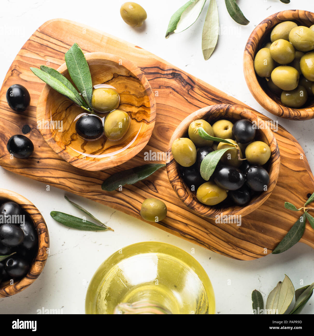 Black and green olives in wooden bowls and olive oil bottle. Top view