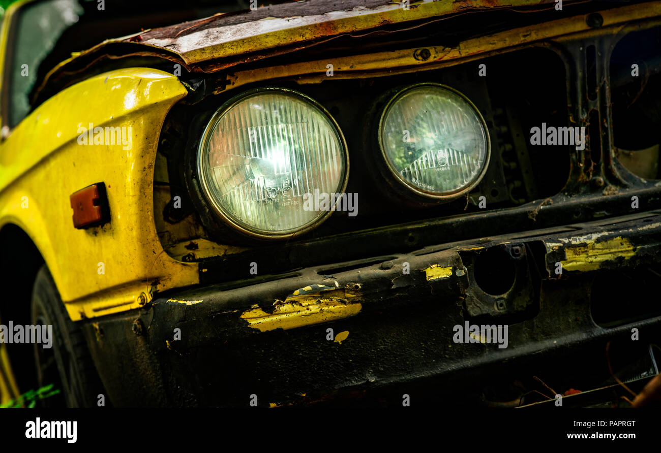 Old wrecked car in vintage style. Abandoned rusty yellow car in the forest. Closeup front view headlights of rusty wrecked abandoned car. The art of a Stock Photo