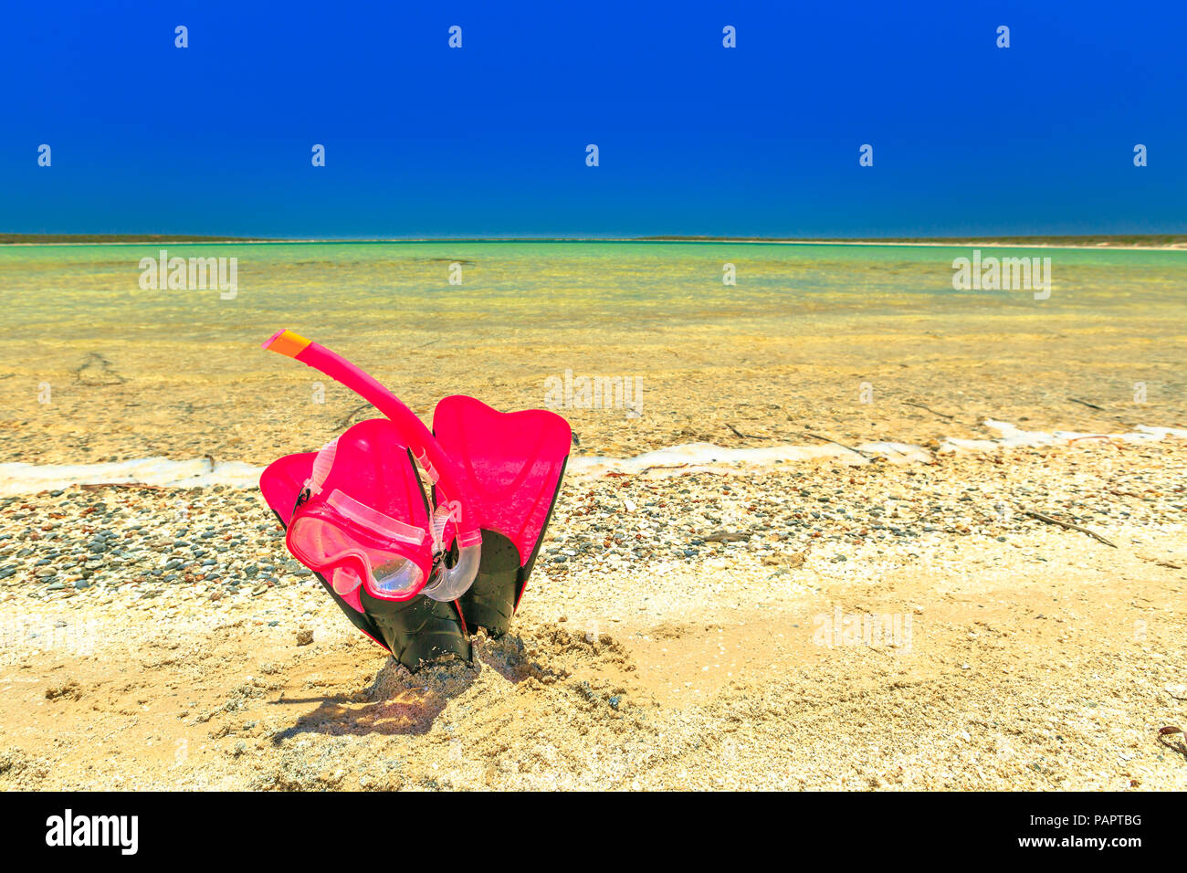 Close-up of scuba mask with fins in pink color on the sand of tropical natural pool of Little Lagoon in Shark Bay, Denham, Western Australia. Copy space with blue sky. Summer water sport. Stock Photo