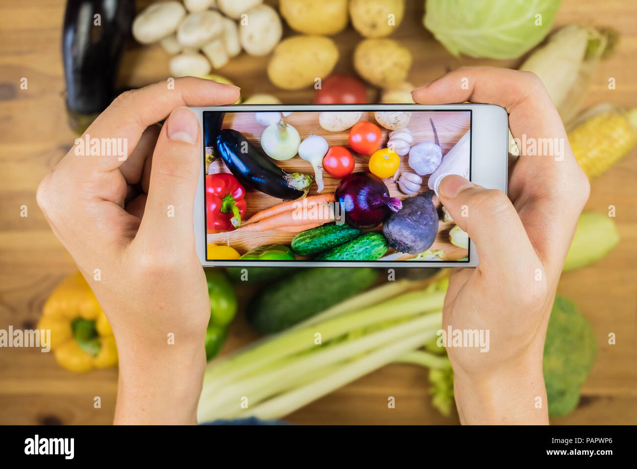 Taking photo of fresh organic vegetables on rustic wood table, top view. Close-up of female hands photographing flat lay of locally grown natural vega Stock Photo