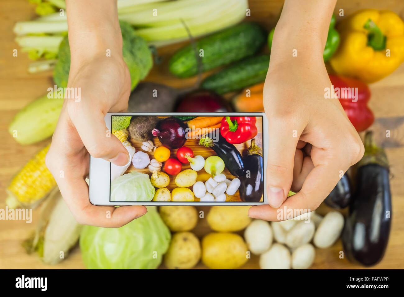 Taking photo of fresh organic vegetables on rustic wood table, top view. Close-up of female hands photographing flat lay of locally grown natural vega Stock Photo