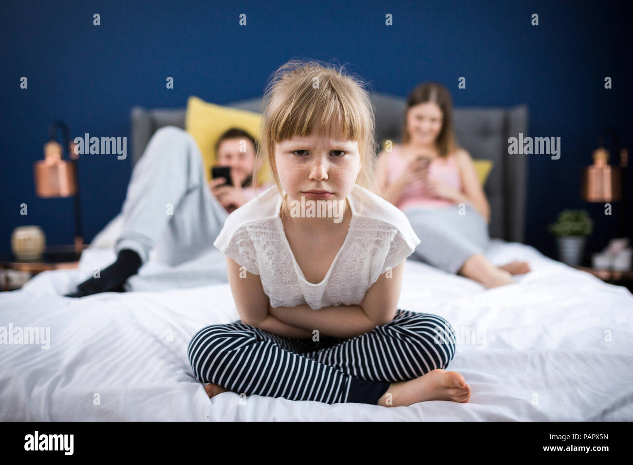 Angry little girl sitting on bed with her parents Stock Photo