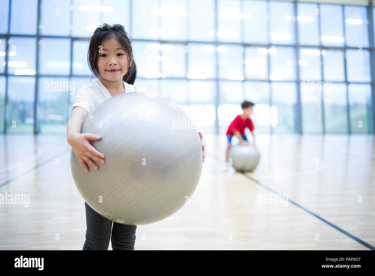 Portrait of smiling schoolgirl holding gym ball in gym class Stock Photo