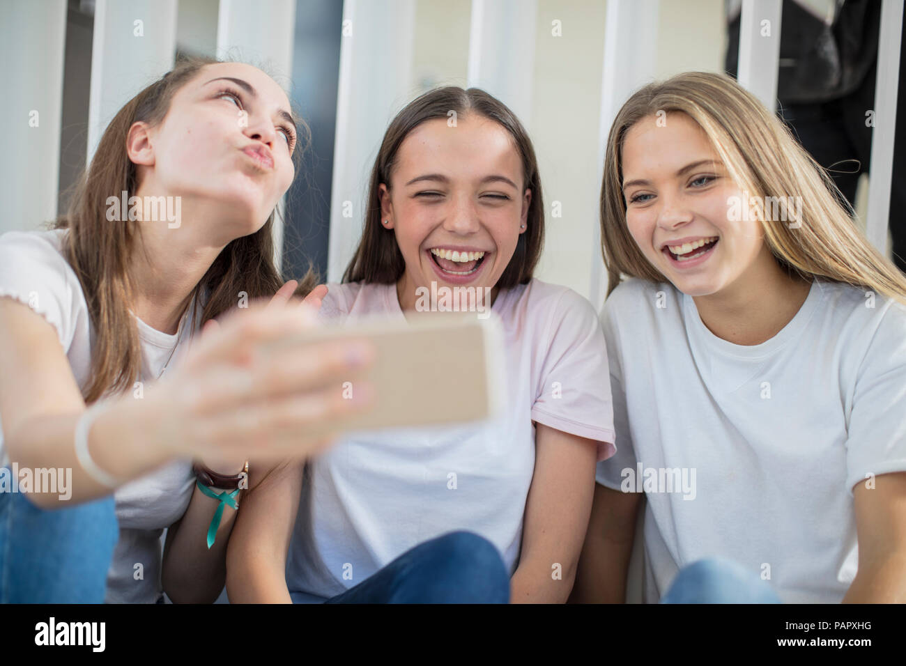 Happy teenage girls sharing cell phone in school Stock Photo