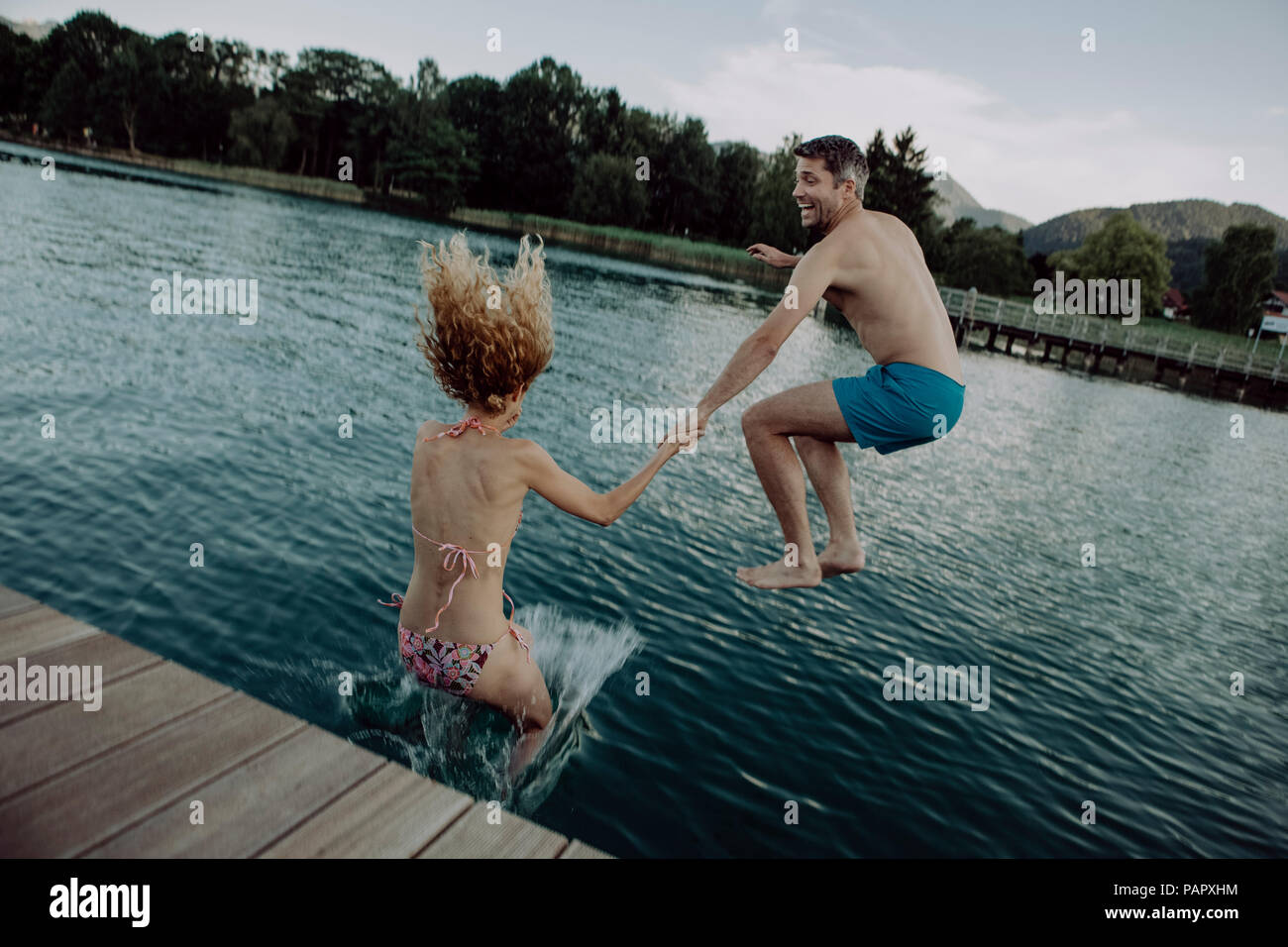 Happy couple jumping hand in hand into swimming lake Stock Photo