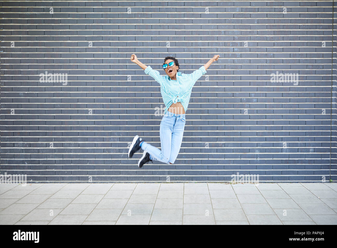 Happy woman jumping in the air in front of grey facade Stock Photo