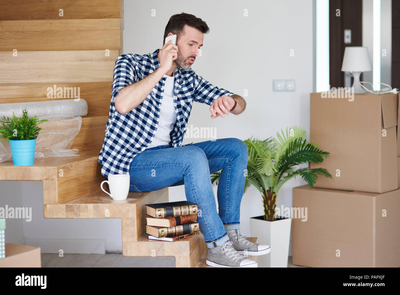 Displeased man moving into new flat talking on cell phone checking the time Stock Photo
