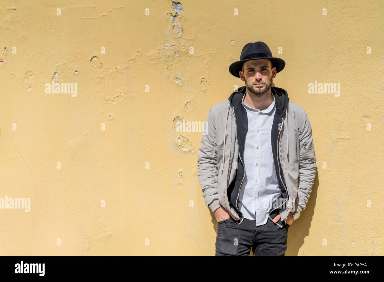 Bearded man wearing black hat, leaning on wall Stock Photo