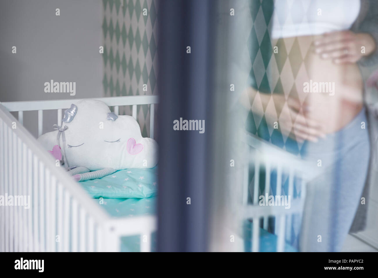 Mirrored pregnant woman, baby bed in the background Stock Photo