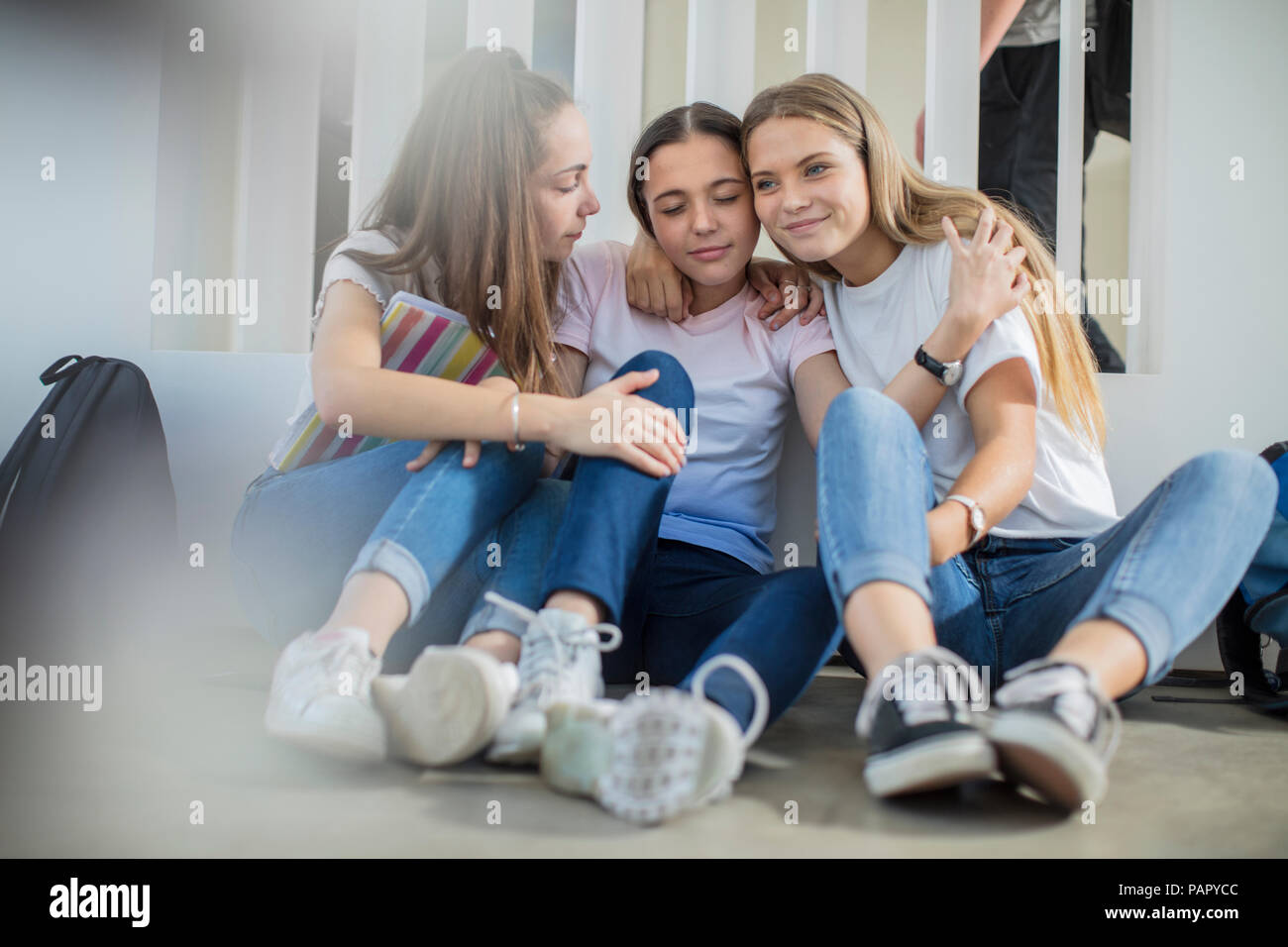 Smiling teenage girls sitting on floor in school hugging Stock Photo