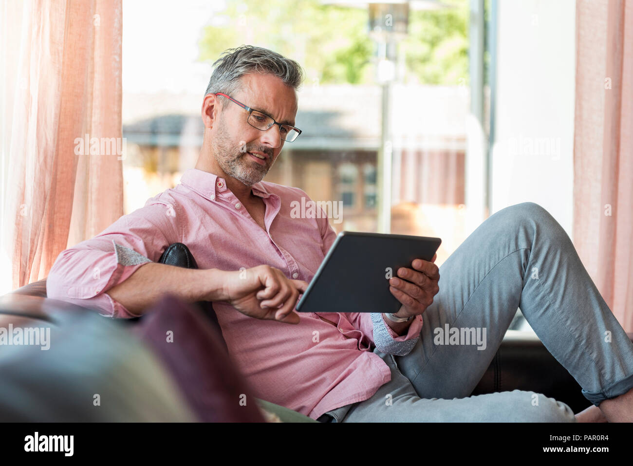 Mature man sitting on couch at home using a tablet Stock Photo