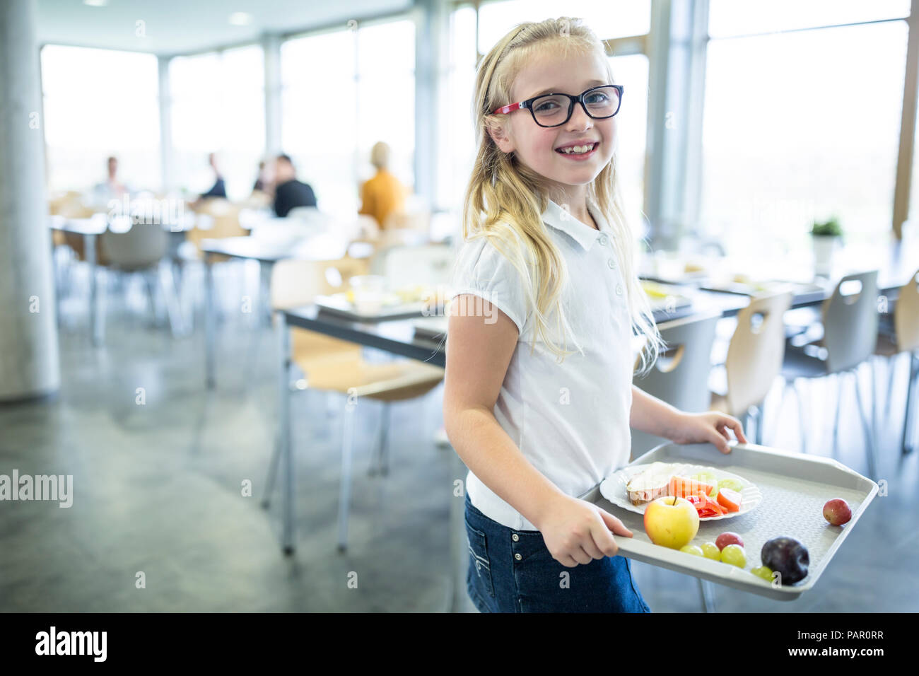 Portrait of smiling schoolgirl carrying tray in school canteen Stock Photo