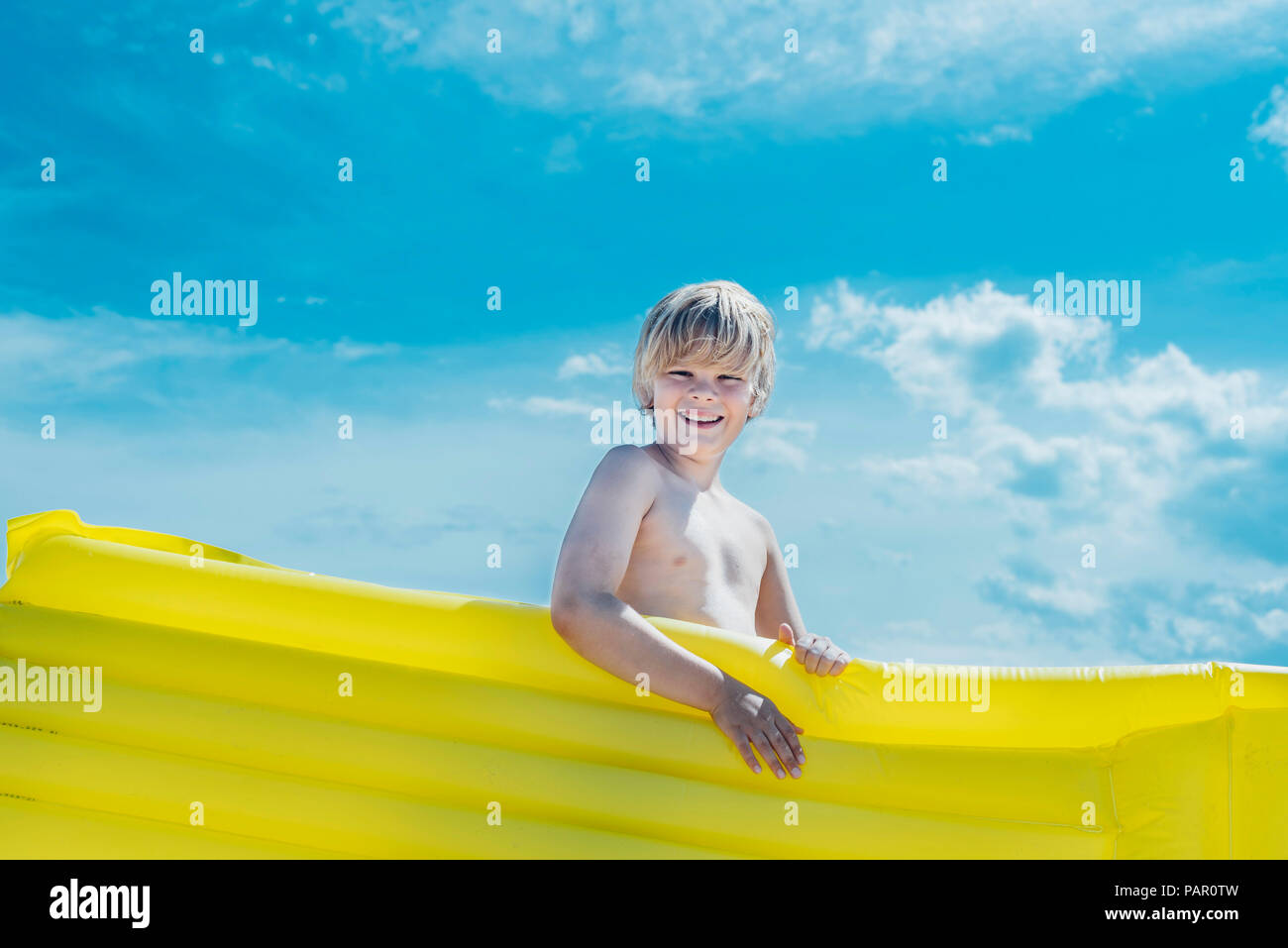 Portrait of happy boy carrying yellow airbed outdoors Stock Photo