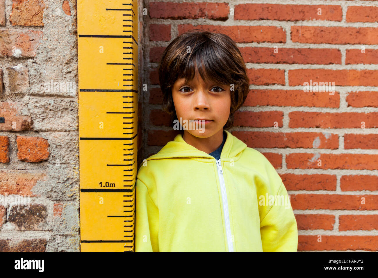 Portrait of sceptical boy leaning against yardstick Stock Photo
