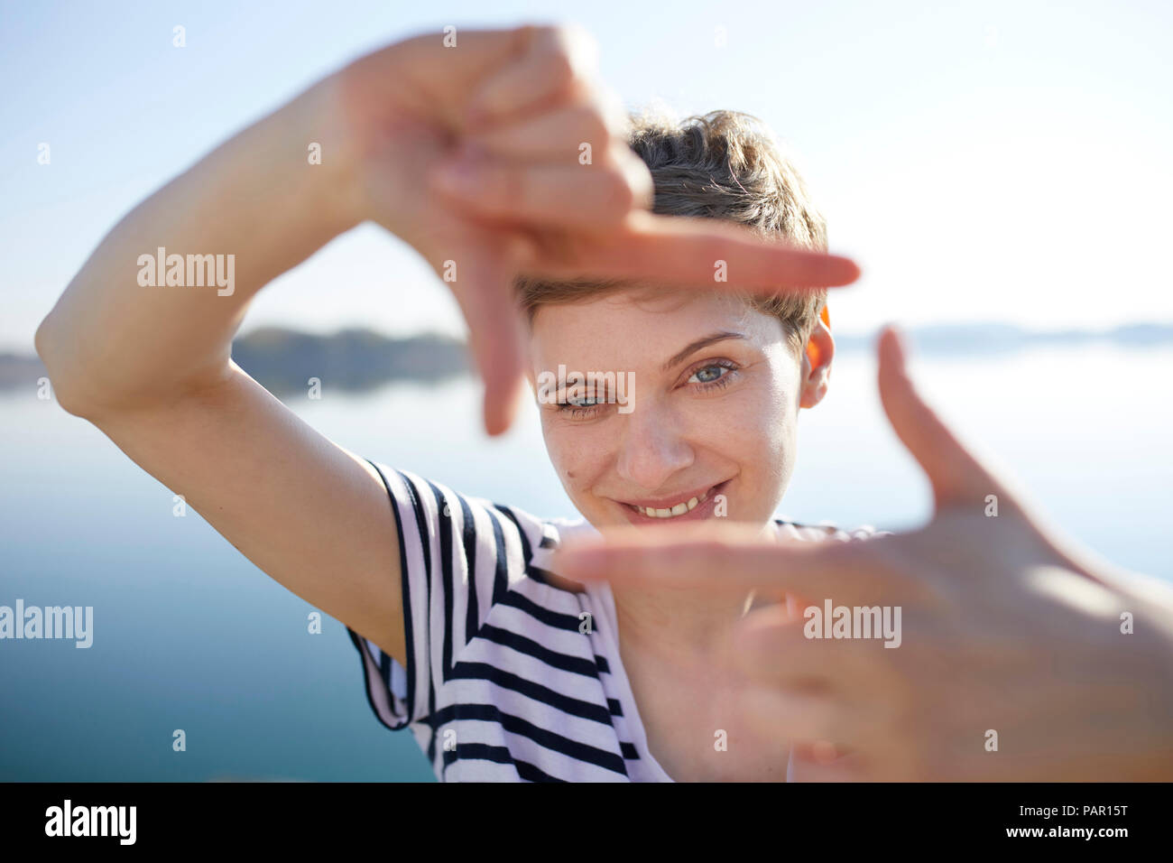 Portrait of woman in front of lake shaping frame with her fingers Stock Photo