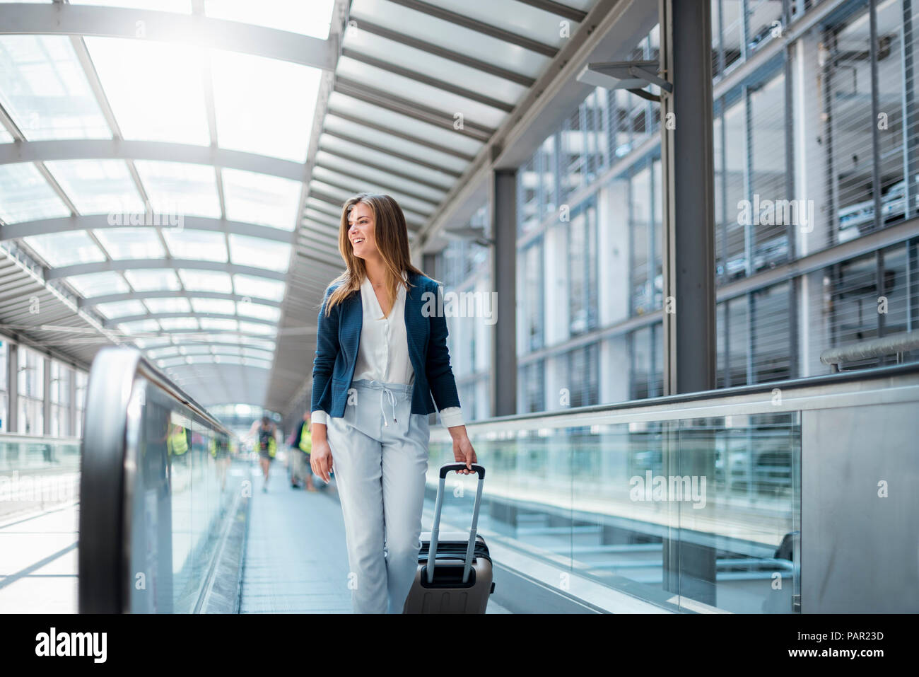 Smiling young businesswoman with baggage on moving walkway Stock Photo