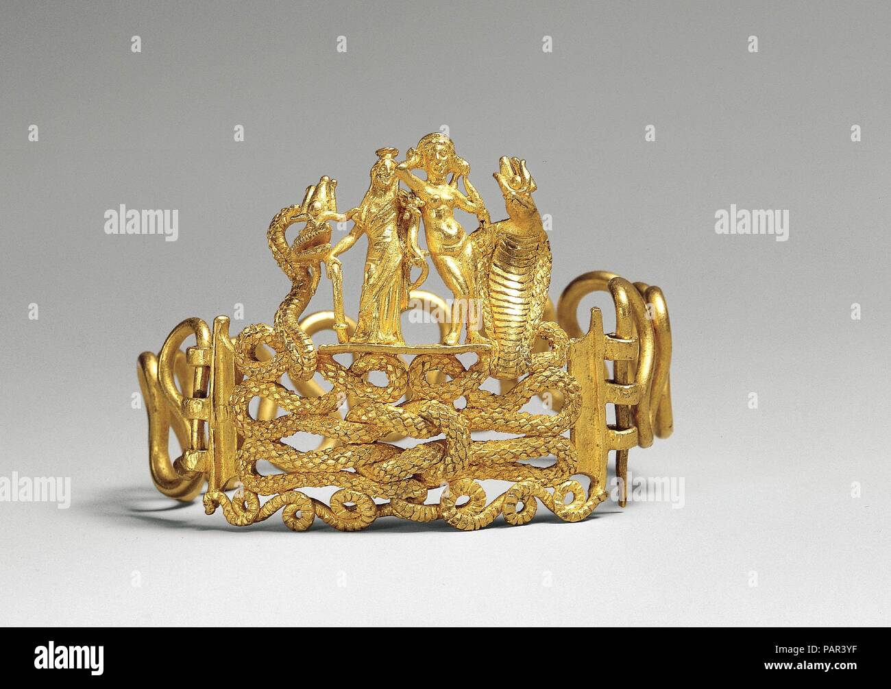 Bracelet with Agathodaimon, Isis-Tyche, Aphrodite, and Terenouthis. Dimensions: 1 9/16 x 2 3/16 in. (4 x 5.5 cm). Date: 1st century B.C.-A.D. 1st century.  Powerful talismans of fertility and good destiny are woven into this rich golden composition. The bodies of two snakes intertwine to form a Herakles knot, the centerpiece of this bracelet. The snake on the left represents Agathodaimon, and the cobra on the right Terenouthis, two agrarian/fertility deities associated with Serapis and Isis, respectively. On the platform between them stand two goddesses, Isis-Tyche (or Isis-Fortuna), a deity c Stock Photo