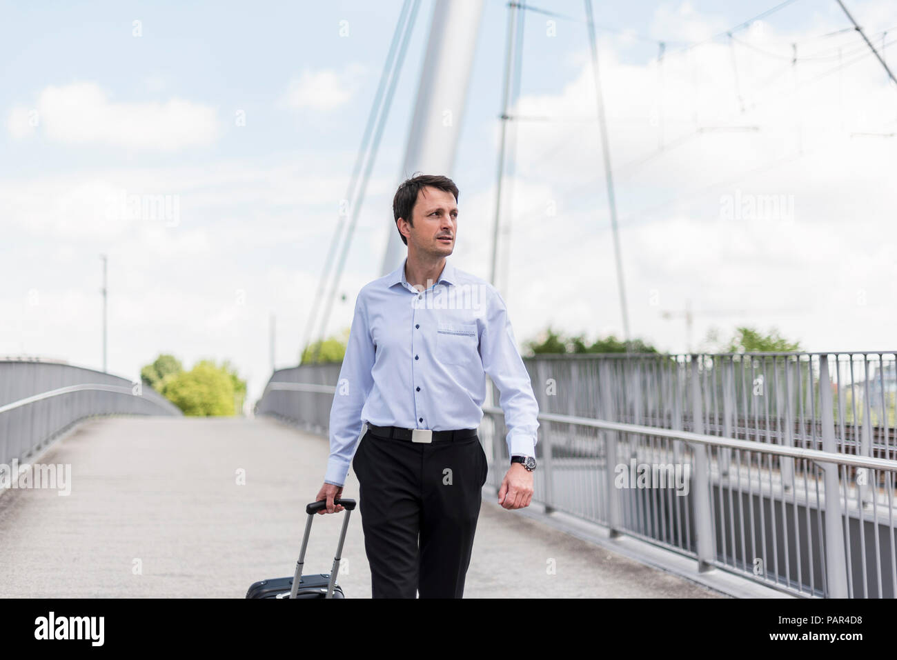 Businessman with rolling suitcase crossing a bridge Stock Photo