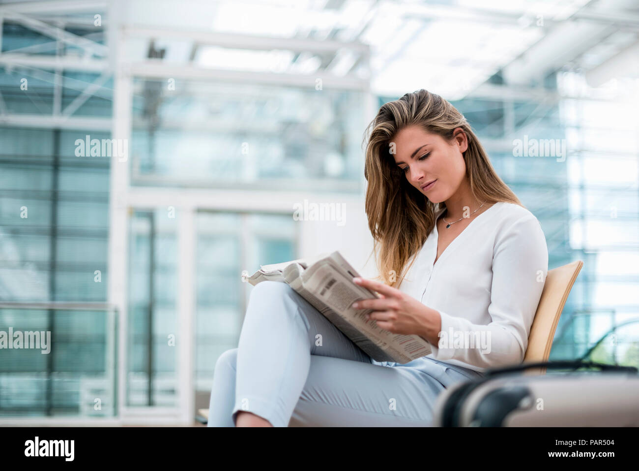 Young businesswoman sitting outdoors with suitcase reading newspaper Stock Photo